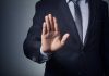 Man in suit with hand raised, signaling stop.