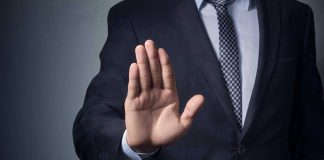 Man in suit with hand raised, signaling stop.