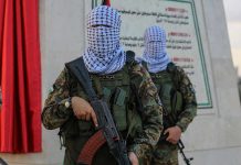 Masked soldiers holding rifles in front of a monument.