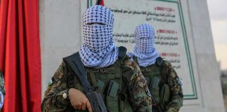 Masked soldiers holding rifles in front of a monument.