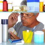 Senior man looking closely at a product in a medicine cabinet filled with various bottles and containers