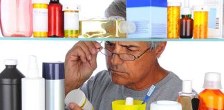 Senior man looking closely at a product in a medicine cabinet filled with various bottles and containers